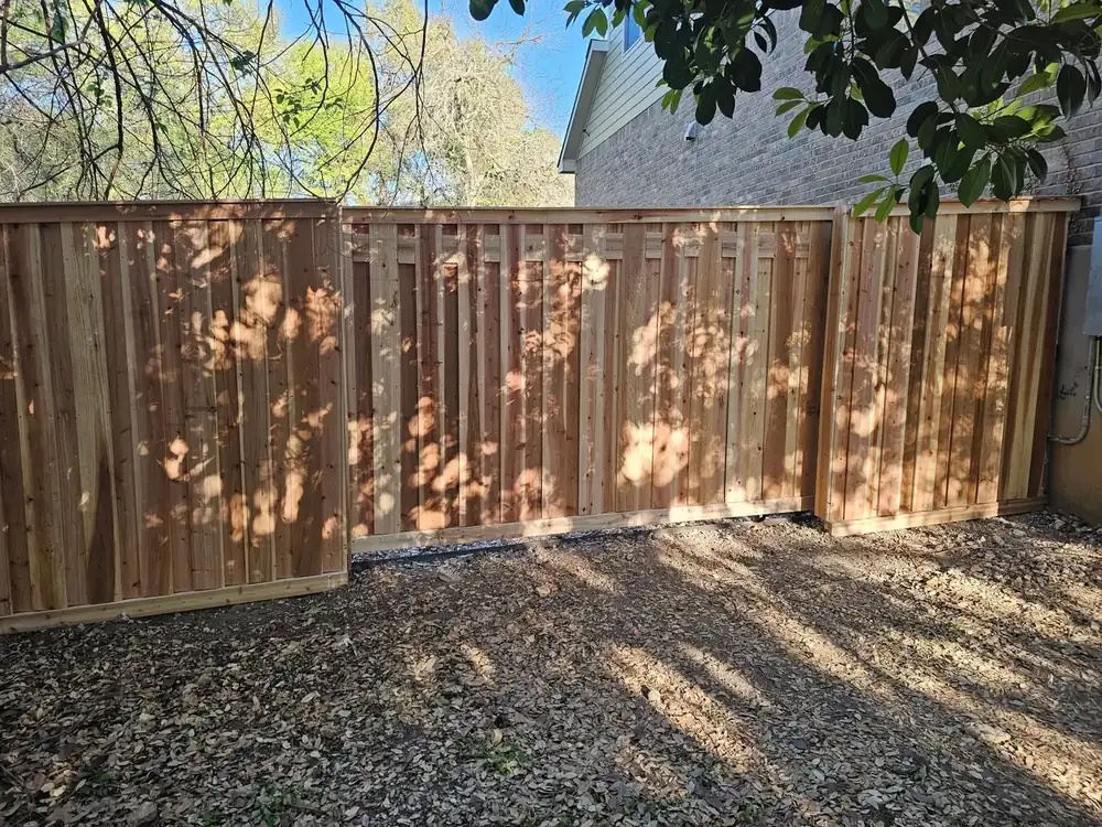 A new cedar privacy fence with a steel frame running along a gravel side yard
